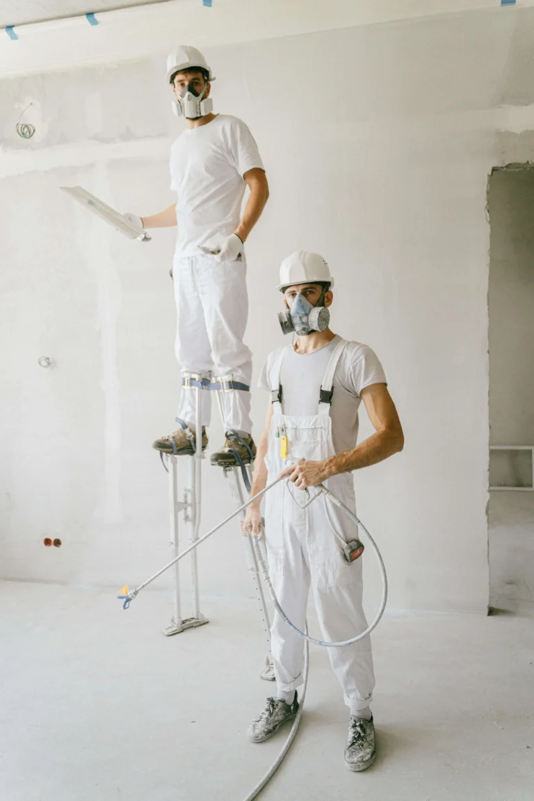 Two professional painters in white coveralls and masks applying fresh paint to interior walls in Vancouver home renovation project